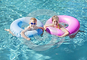 Two cute kids playing on inflatable tubes in a swimming pool on a sunny day