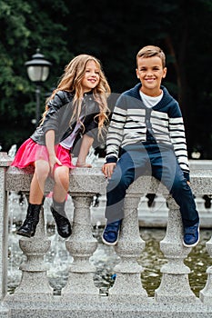 Two cute kids are sitting on the railing. Marble-stone fountain.