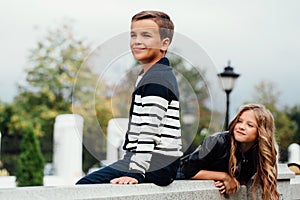 Two cute kids are sitting on the railing. Marble-stone fountain.