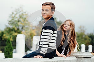 Two cute kids are sitting on the railing. Marble-stone fountain.