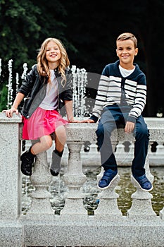 Two cute kids are sitting on the railing. Marble-stone fountain.