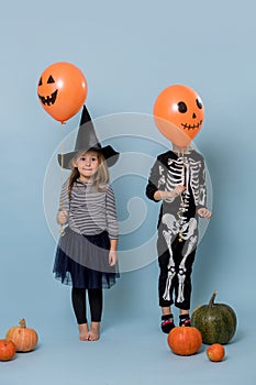 Two cute kids in witch and skeleton costumes holding orange halloween balloons