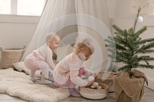 Two cute little baby girls play in a spacious bright minimalistic children`s room.