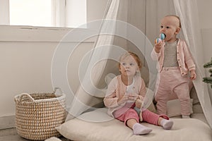 Two cute little baby girls play in a spacious bright minimalistic children`s room.