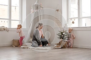 Two cute little baby girls play with their mom in a bright minimalistic children`s room.