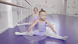 Two cute little ballerinas girls stretching at ballet class doing splits