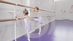 Two cute little ballerinas stretching at ballet school together