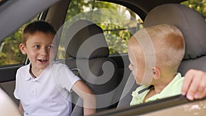 Two cute little boys are sitting at the wheel of their father's car and talking.