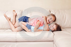 Two cute little Caucasian girls siblings playing at home. Adorable children kids lying hugging on a couch together. Authentic