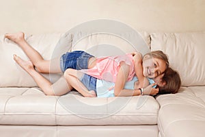 Two cute little Caucasian girls siblings playing at home. Adorable children kids lying hugging on a couch together. Authentic