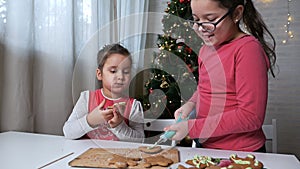 Two cute little children, girls-sisters, prepare gingerbread for Christmas on the background of a beautiful Christmas