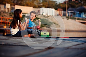 Two cute little friends, boy and girl talking, drinking tea, eating sandwiches and fishing on a lake in a sunny summer day