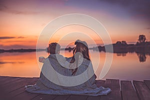 Two cute little friends, boy and girl talking and drinking tea while sitting covered with blanket by the lake during beautiful