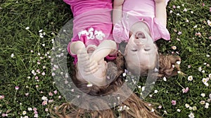 Two cute little girl lying upside down on meadow grass and flowers making air kiss and waving hand