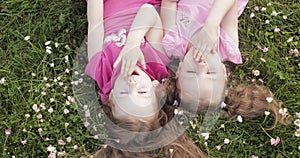 Two cute little girl lying upside down on meadow grass and flowers making air kiss and waving hand