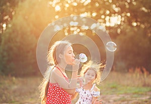 Two Cute Little Girls blowing soap bubbles outdoor at summer day - happy childhood