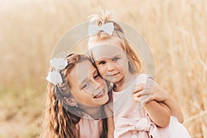 Two cute little girls in dresses hugging in nature in the summer