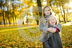 Two cute little girls having fun on beautiful autumn day. Happy children playing in autumn park. Kids gathering yellow fall foliag