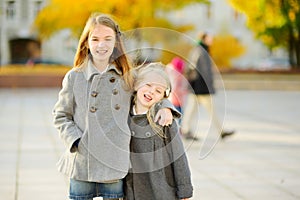 Two cute little girls having fun on beautiful autumn day. Happy children playing in autumn park. Kids gathering yellow fall foliag