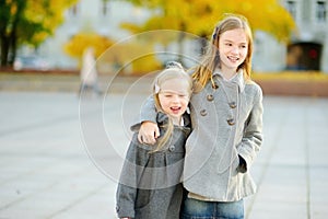 Two cute little girls having fun on beautiful autumn day. Happy children playing in autumn park. Kids gathering yellow fall foliag