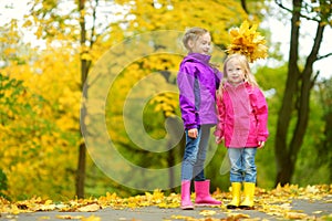 Two cute little girls having fun on beautiful autumn day. Happy children playing in autumn park. Kids gathering yellow fall foliag