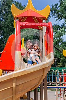 Two cute little girls having fun on a playground outdoors in summer
