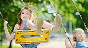 Two cute little girls having fun on a playground outdoors on summer day
