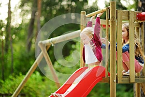 Two cute little girls having fun on a playground outdoors on warm summer day