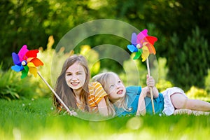 Two cute little girls holding colorful toy pinwheels on sunny summer day
