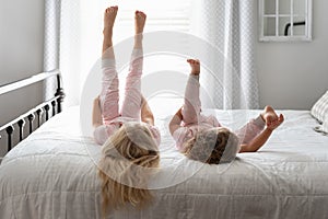 Two cute little girls lying on a big white bed with their feet in the air