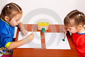 Two cute little girls are painting with gouache