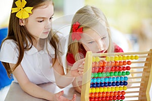 Two cute little girls playing with abacus at home. Big sister teaching her sibling to count.