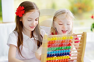 Two cute little girls playing with abacus at home. Big sister teaching her sibling to count.