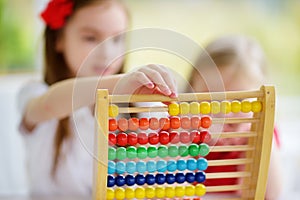 Two cute little girls playing with abacus at home. Big sister teaching her sibling to count.