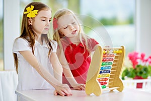 Two cute little girls playing with abacus at home. Big sister teaching her sibling to count.