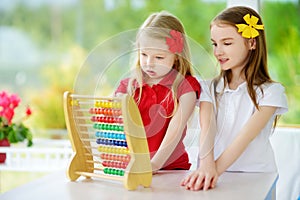 Two cute little girls playing with abacus at home. Big sister teaching her sibling to count. Smart child learning to count.