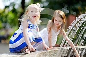 Two cute little girls playing with a city fountain on hot summer day