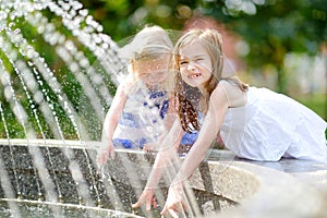 Two cute little girls playing with a city fountain on hot summer day
