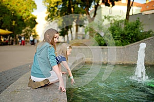 Two cute little girls playing by city fountain on hot and sunny summer day. Children having fun with water in summer