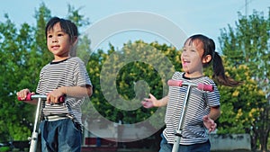 Two cute little girls riding scooter on road in park outdoors on summer day. Kids play outdoors with scooters. Active leisure and