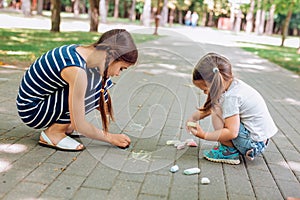 Two cute little girls sitting and drawing with chalk on asphalt in park