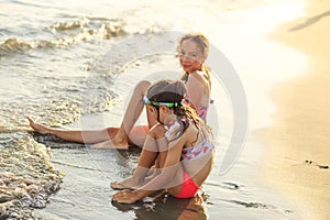 Two Cute Little Girls sitting at the sea and playing with waves  at sunset.  Summer Sunny Day, Ocean Coast, happy Kids concept