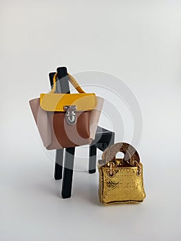 Two cute little miniature purses one on a black chair the other leaning on it