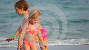 Two cute little sibling girls in pink swimsuits are playing on the beach