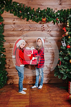 Two cute little sisters with big red present gift box near Christmas tree at home.