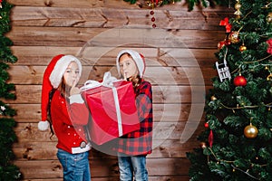 Two cute little sisters with big red present gift box near Christmas tree at home.