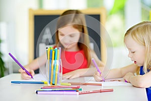 Two cute little sisters drawing with colorful pencils at a daycare
