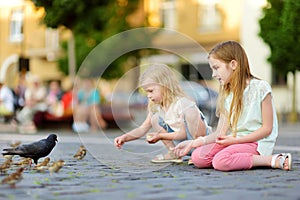 Two cute little sisters feeding birds on summer day. Children feeding pigeons and sparrows outdoors.