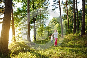 Two cute little sisters having fun during forest hike on beautiful summer day. Active family leisure with kids.