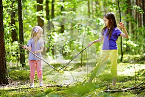 Two cute little sisters having fun during forest hike on beautiful summer day. Active family leisure with kids.